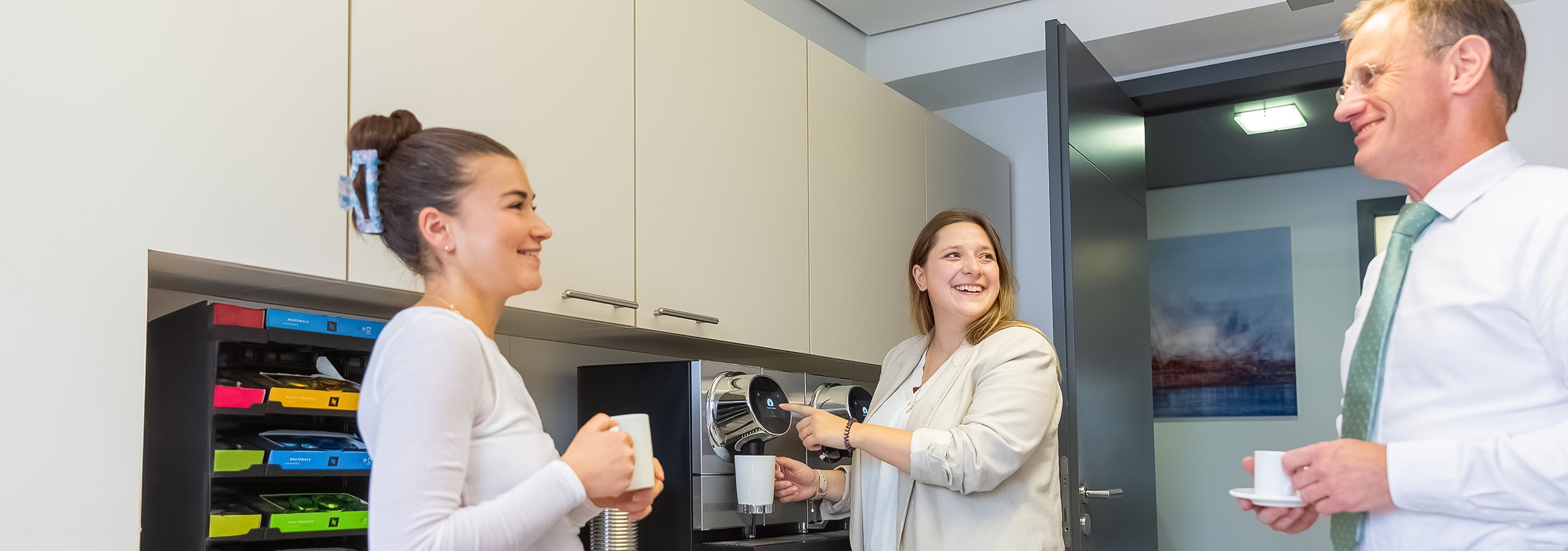 In der Kaffeeküche des Notariats unterhalten sich drei Teammitglieder und lachen dabei